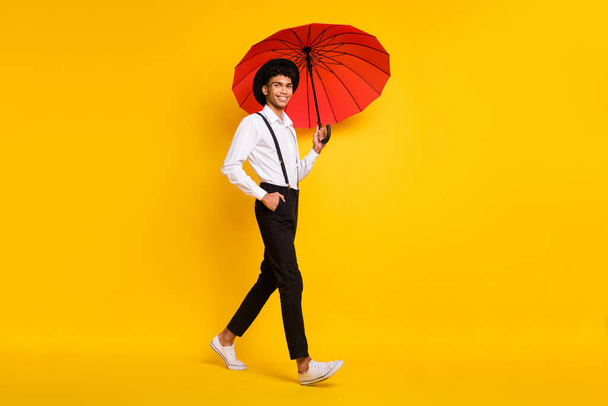 Full length photo portrait of african american man walking with red umbrella isolated on vivid yellow colored background - Photo, Image