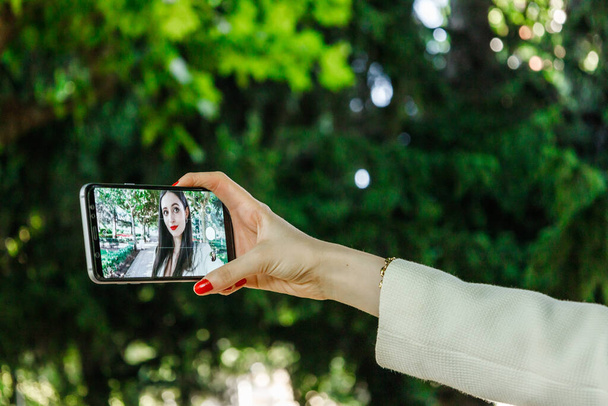 Detailní záběr chytré obrazovky drží bílé ženy ruce s červenými nehty, zatímco ona bere selfie - Fotografie, Obrázek