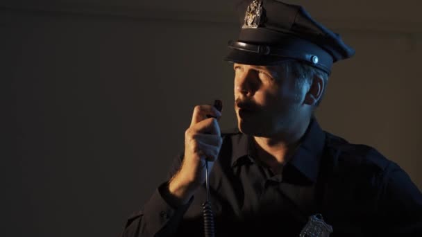 een mannelijke politieagent spreekt op een walkietalkie terwijl hij een close-up portret patrouilleert - Video