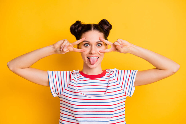 Photo of childish adorable young woman wear striped t-shirt showing tongue v-signs cover eyes isolated yellow color background - Fotó, kép