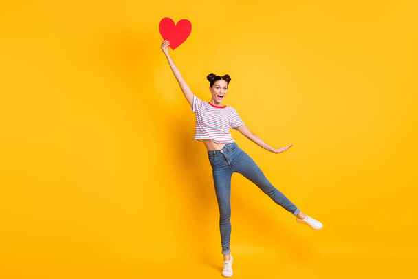 Photo of excited charming young lady wear striped t-shirt holding big red heart isolated yellow color background - Фото, зображення