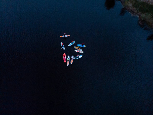 Touristen treiben auf SUP-Boards im blauen Meer. Blick von oben auf eine Gruppe von Menschen auf SUP-Boards, die in ruhiger, klarer See treiben - Foto, Bild