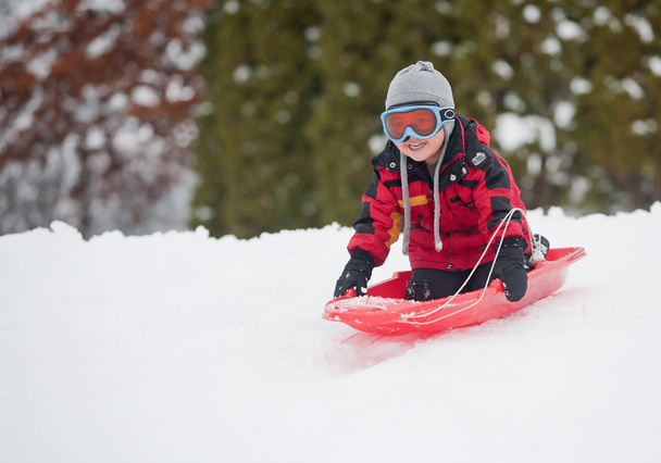 A young boy shows his excitement sledding down a hill in winter. - Photo, Image