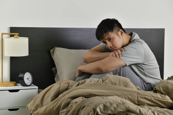 Depressiver junger Asiate, der im Bett sitzt, kann vor Schlaflosigkeit nicht schlafen - Foto, Bild