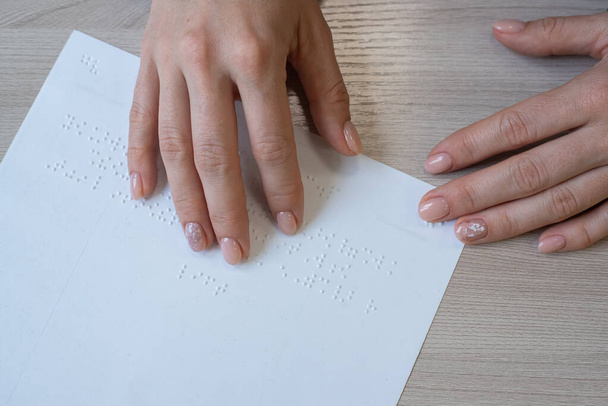 Close-up woman reads the text to the blind. Womans hands on paper with braille code. - 写真・画像
