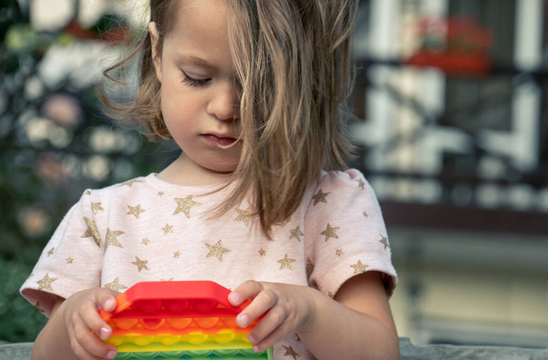 Portrét koncentrované roztomilé holčičky hrající si venku na popovou hračku, na dvoře malého domku pro hosty.  - Fotografie, Obrázek