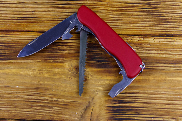 Červená univerzální kapesní nůž na rustikálním dřevěném pozadí. Horní pohled - Fotografie, Obrázek