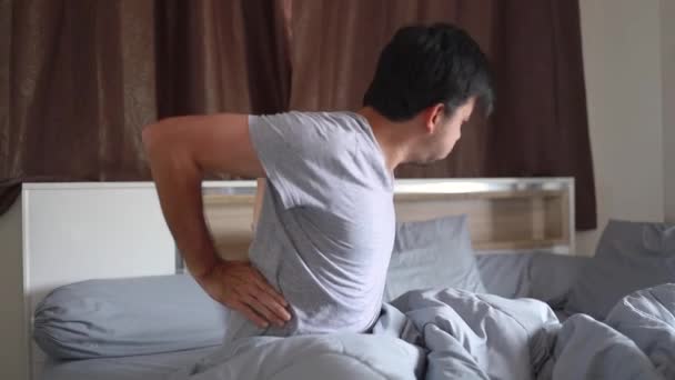 Молодой азиат с болью в спине на кровати дома, проблемы со здоровьем - Кадры, видео