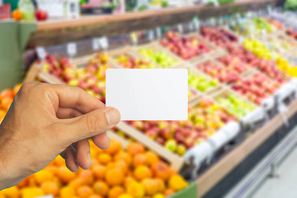 Üres műanyag élelmiszerkártya a kezében a szupermarket hátterében. Élelmiszer-kártya kedvezmények és promóciók üzletekben és szupermarketekben - Fotó, kép