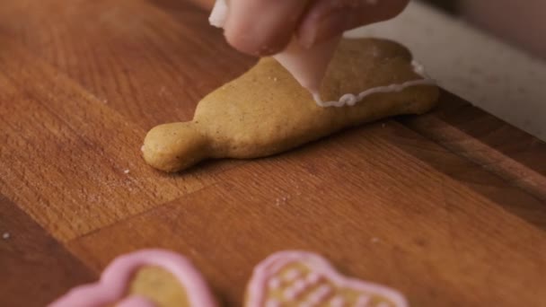 Woman decorates a gingerbread in the shape of bell on the wooden desk with icing. Christmas tradition.  - Footage, Video