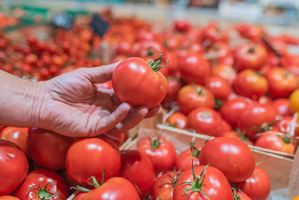 男性の手は野菜市場のカウンターで熟したトマトを選ぶ - 写真・画像