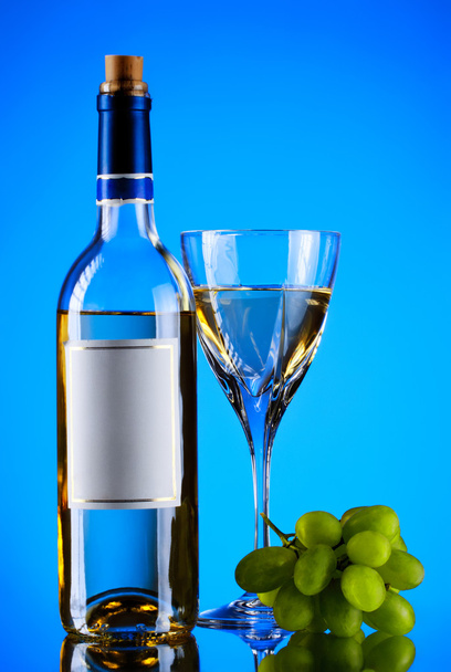 Bottle and glass of wine, grape bunch, blue background - Фото, изображение
