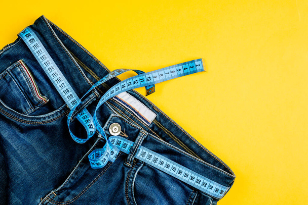 El concepto de un estilo de vida y una dieta saludables. Pantalones vaqueros azules con cinta métrica azul en lugar de cinturón. - Foto, imagen