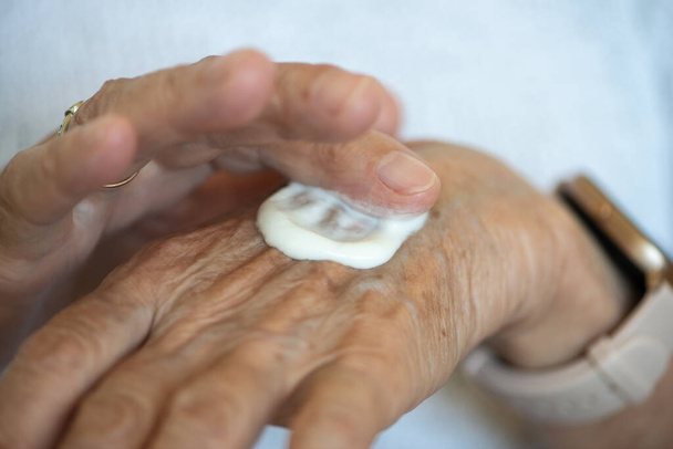 Las mujeres mayores se ponen crema en las manos. De cerca. Adultos mayores rutina diaria. - Foto, imagen