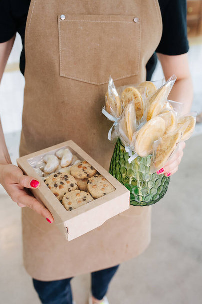 Cookies in a windowed box and on sticks in a vase, held by confectioner in his hands. He is wearing beige apron. - Foto, Bild