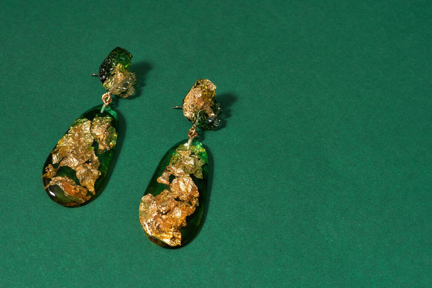 Top view of dangle earrings made of epoxy resin with golden foil inside isolated over green background - Foto, Imagen