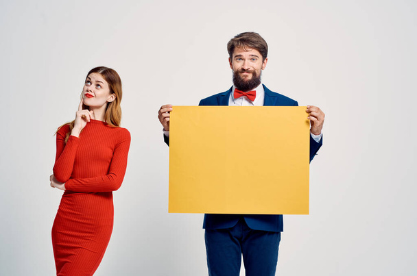 man en vrouw staan zij aan zij reclame gele mockup poster licht achtergrond - Foto, afbeelding