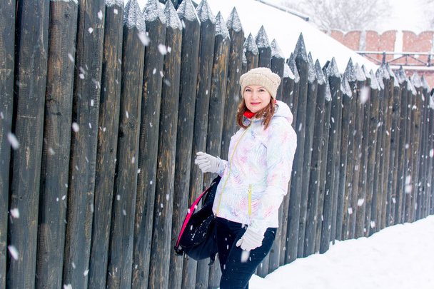 Russia, Tula. January 9, 2021. Portrait of a beautiful woman tourist on the background of a wooden house and a fence in winter. - Фото, изображение