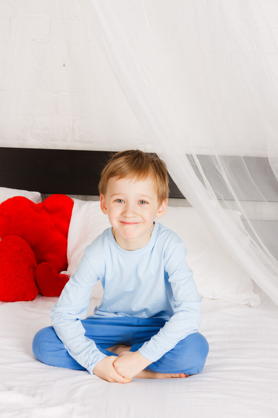 Mosolygó fiú ül egy ágy, egy kényelmes helyzetben - Fotó, kép