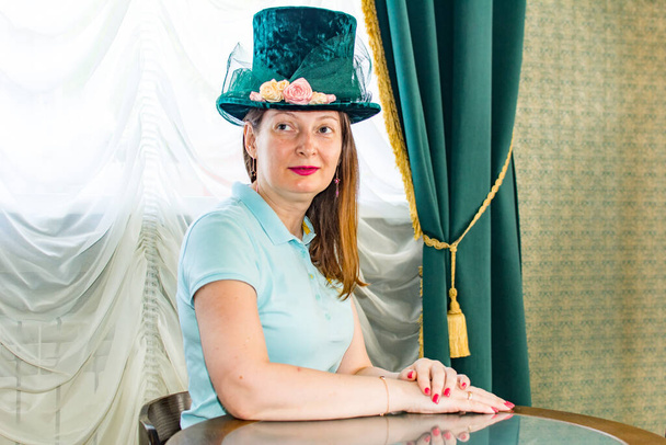 Красивая женщина в старой изящной шляпе сидит за столом - Фото, изображение