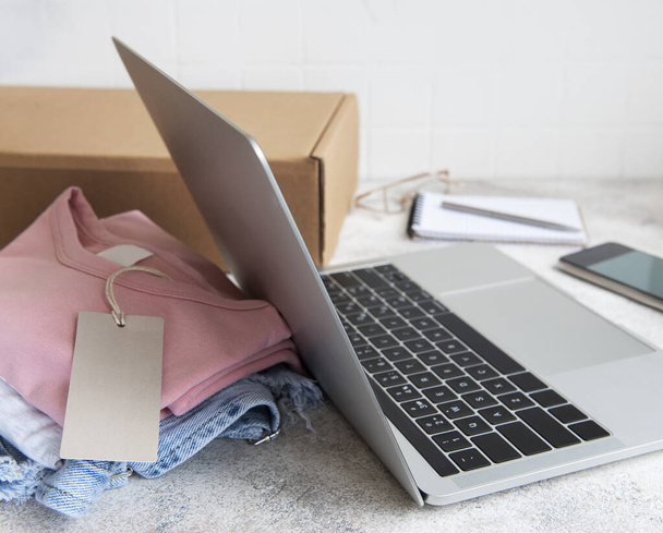 Online-Einkaufskonzept. Ein Laptop und ein Satz Damenbekleidung in einem Karton. Lieferung von Kleidung. - Foto, Bild