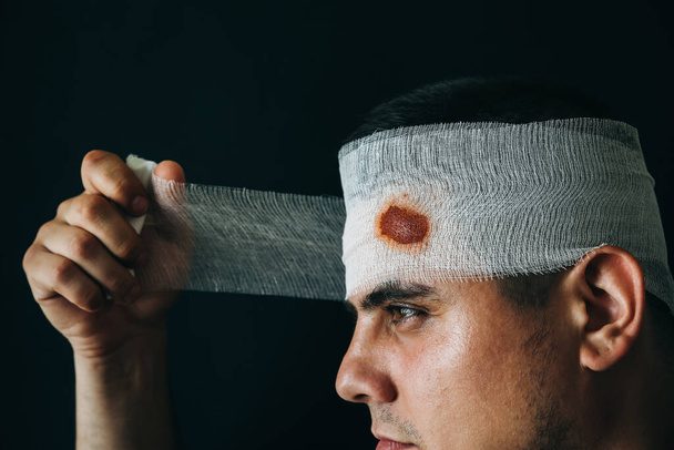 Man with a bondage on the head. Bleeding round wound. Injured in the fight. - Photo, Image