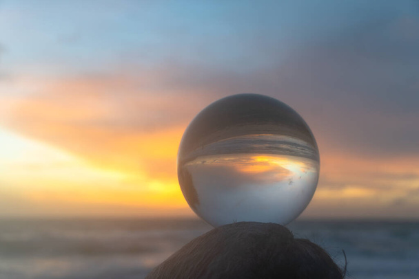 hermosa nube y puesta de sol de oro dentro de bola de cristal colocado en una madera al lado de la playa - Foto, imagen