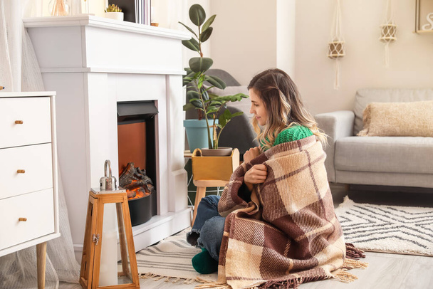 Young woman sitting near fireplace at home. Concept of heating season - Photo, image