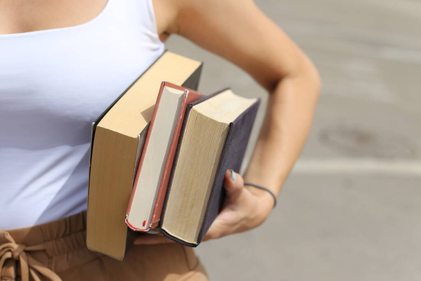 Η μαθήτρια κουβαλάει βιβλία κάτω από το χέρι της. - Φωτογραφία, εικόνα