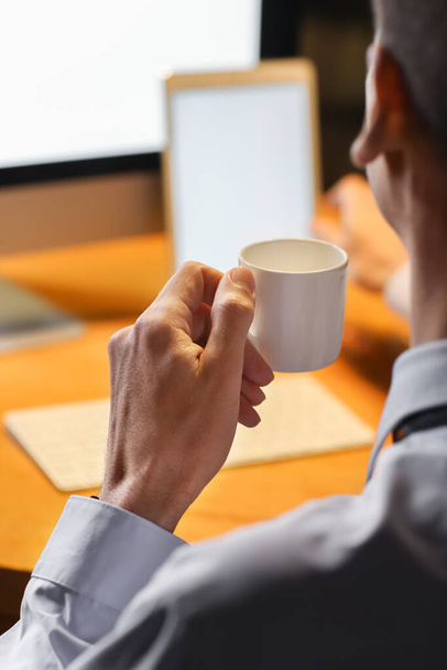 Geschäftsmann trinkt Kaffee, während er spät abends im Büro arbeitet - Foto, Bild
