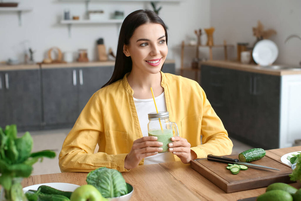 Молода жінка зі склянкою здорової зеленої смуги на кухні
 - Фото, зображення