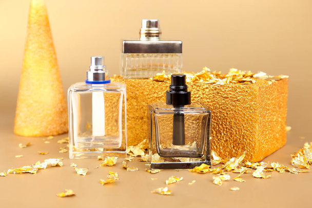 Three unbranded perfume spray bottles, pieces of gold paper and golden rectangular shape on golden background. Front view, mockup, template. - Photo, Image
