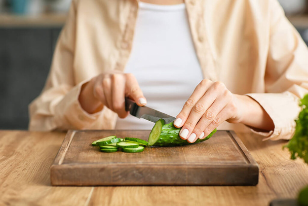 Молода жінка, що ріже огірок на кухні
 - Фото, зображення