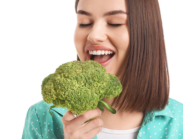 Young woman eating fresh broccoli on white background, closeup - 写真・画像