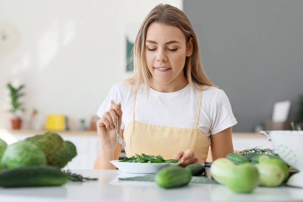 Young woman eating fresh salad in kitchen - Photo, Image