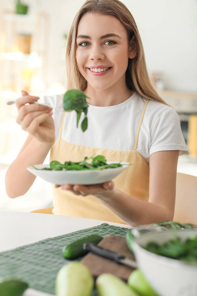 Nuori nainen syö tuoretta salaattia keittiössä - Valokuva, kuva