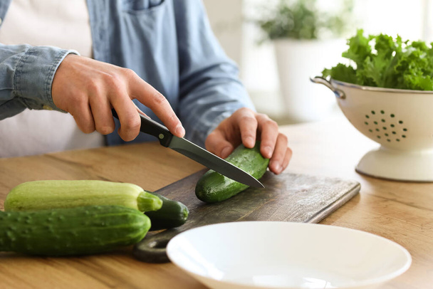 Young man cutting cucumber in kitchen, closeup - Photo, Image