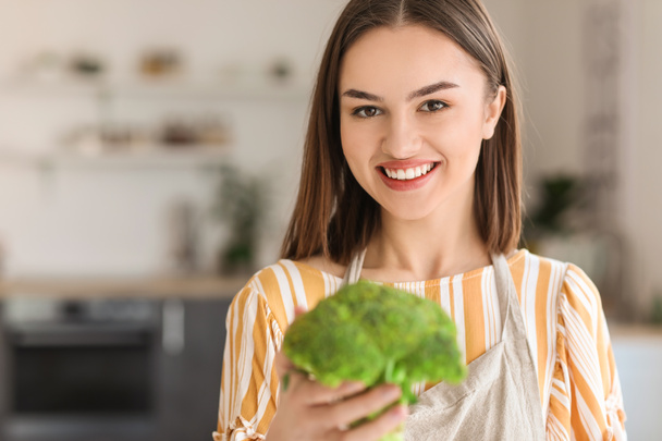 Young woman with fresh broccoli in kitchen, closeup - Foto, imagen