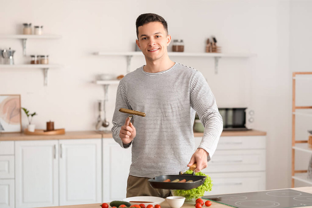 Young man frying tasty sausages in kitchen - Foto, Bild