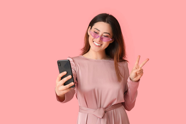 Stylish young Asian woman taking selfie on color background - Photo, Image