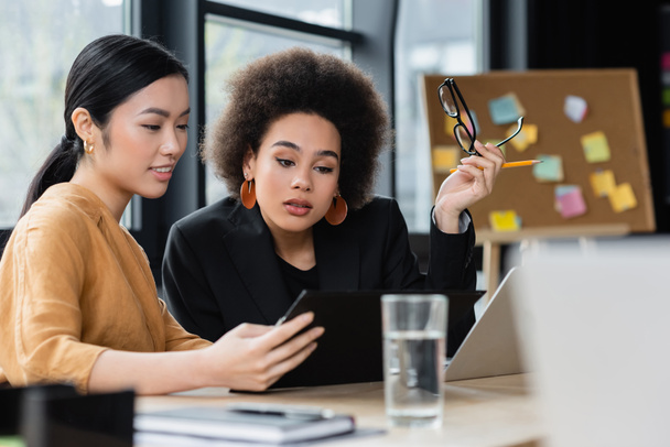 mujeres de negocios interracial mirando el portapapeles mientras trabajan en la oficina - Foto, Imagen