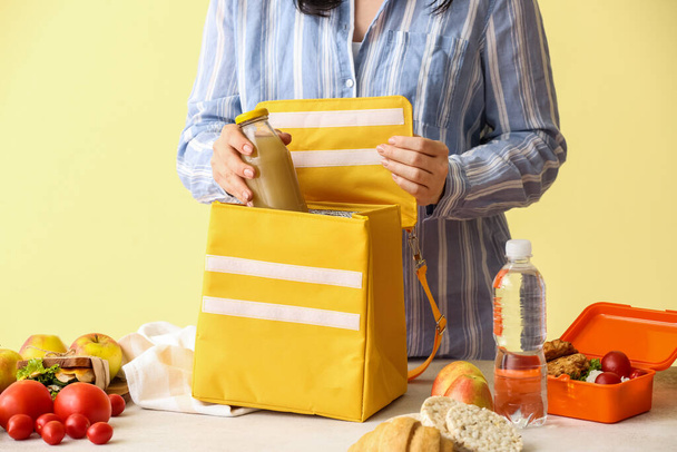 Vrouw verpakking fles sap in lunch doos zak op kleur achtergrond - Foto, afbeelding