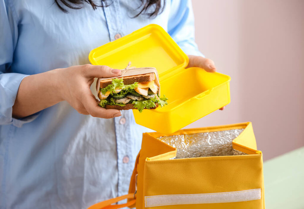 Frau verpackt Mahlzeit in Lunchbox-Tasche auf farbigem Hintergrund, Nahaufnahme - Foto, Bild