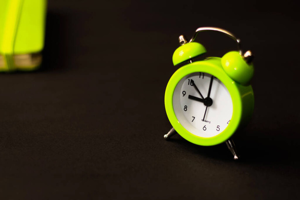Light green alarm clock on a black background with notebook. Time minimalistic concept. At nine o'clock in the morning Selective focus - Photo, Image