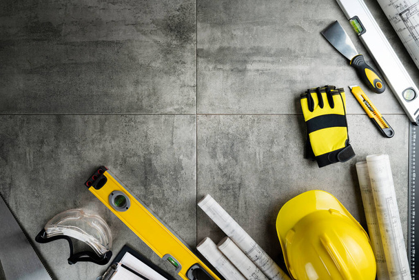 Contractor theme. Plans, tool kit of the contractor, yellow hardhat and libella. Gray tiles background. - Photo, Image