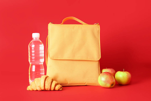 Обідня сумка, пляшка води, яблука та круасан на кольоровому фоні
 - Фото, зображення