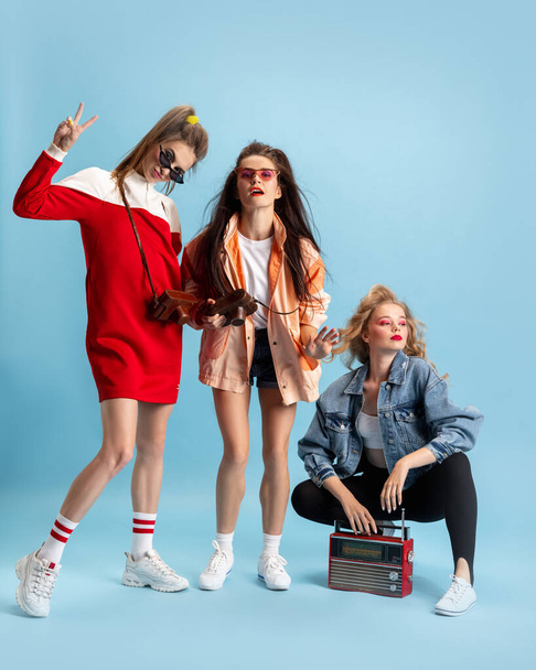 Pretty young women in retro 90s fashion style, outfits posing isolated over blue studio background. Concept of eras comparison, beauty, fashion and youth. - Fotoğraf, Görsel