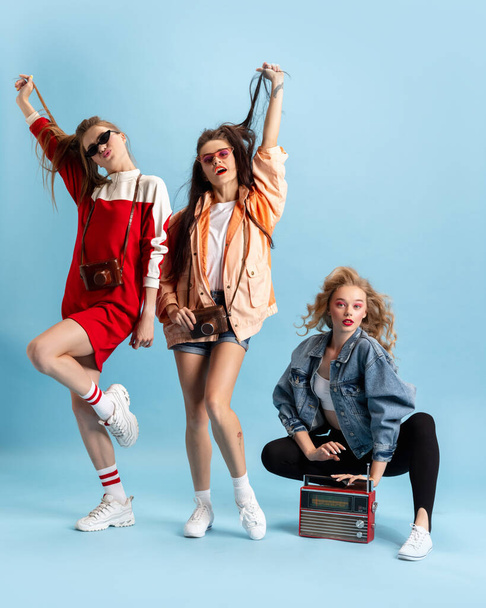 Pretty young women in retro 90s fashion style, outfits posing isolated over blue studio background. Concept of eras comparison, beauty, fashion and youth. - Fotó, kép