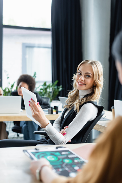 mujer de negocios rubia con tableta digital sonriendo cerca de colega en primer plano borrosa - Foto, Imagen