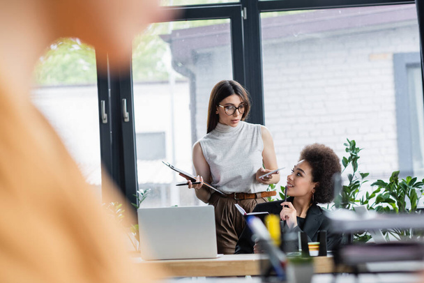 young interracial businesswomen talking in office on blurred foreground - Foto, Imagen